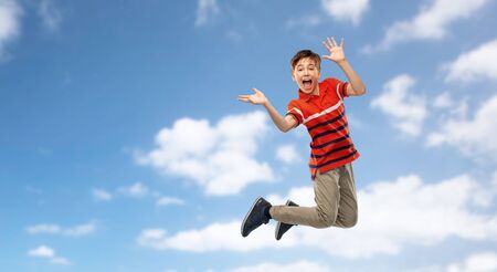 happy smiling young boy jumping in air over skyの写真素材