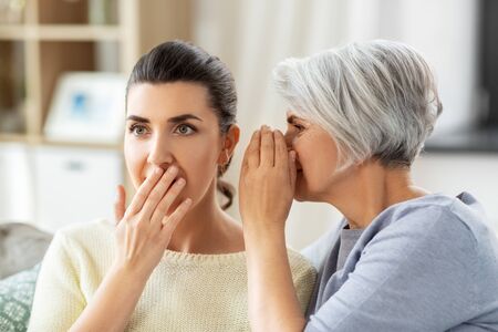 senior mother whispering secret to adult daughterの写真素材