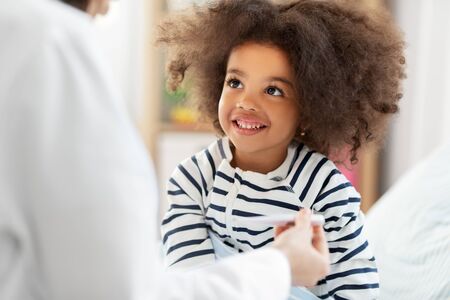 doctor showing thermometer to smiling sick girlの写真素材