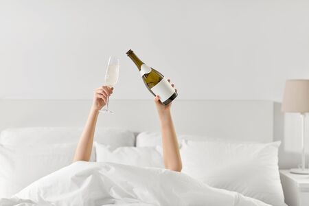 hands of woman lying in bed with champagneの写真素材