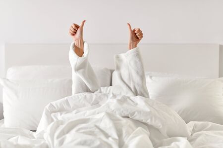 hands of woman lying in bed and showing thumbs upの写真素材