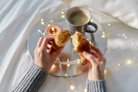 hands of woman eating croissant with coffee in bedの写真素材
