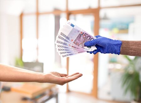 finance, payment and pandemic concept - close up of one hand in medical glove giving money to...