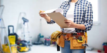 repair, construction and building concept - close up of woman or builder with clipboard, pencil and...