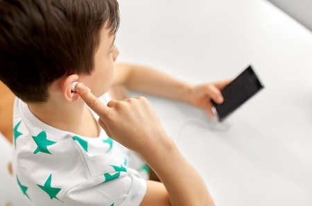 children, technology and people concept - close up of boy with smartphone and earphones listening to...