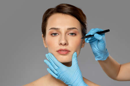 cosmetology, plastic surgery and beauty concept - beautiful young woman and hands with marker over grey background and snowの写真素材