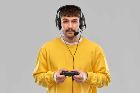 technology, gaming and people concept - young man or gamer in headphones with gamepad playing and...