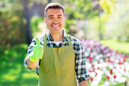 happy man in apron showing thumbs up at gardenの写真素材