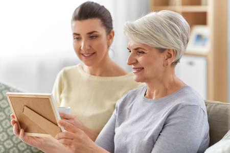 adult daughter and old mother with photo at home