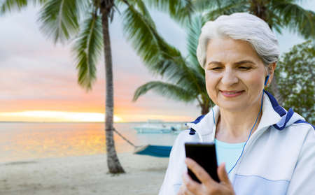 fitness, sport and healthy lifestyle concept - senior woman with earphones listening to music on...