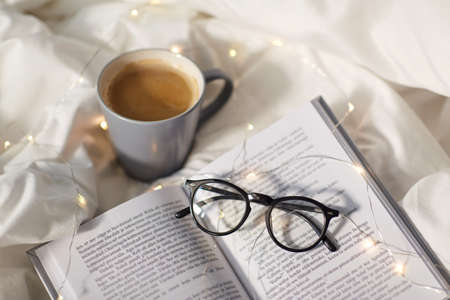 cup of coffee, book, glasses and garland in bedの写真素材