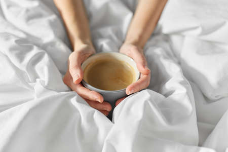 hands of woman with cup of coffee in bedの写真素材