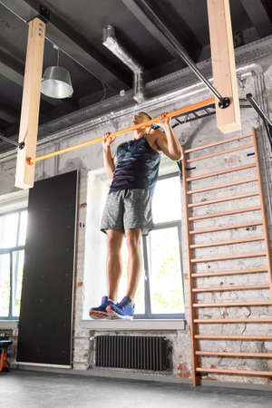 man exercising on bar and doing pull-ups in gym