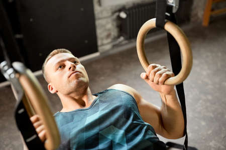 man doing exercising on gymnastic rings in gym