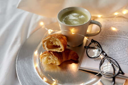 croissants, matcha tea, book and glasses in bed