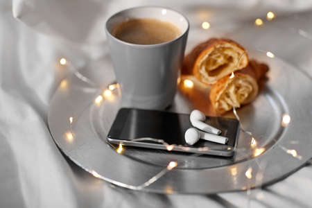 smartphone, earphones, coffee and croissant in bedの写真素材