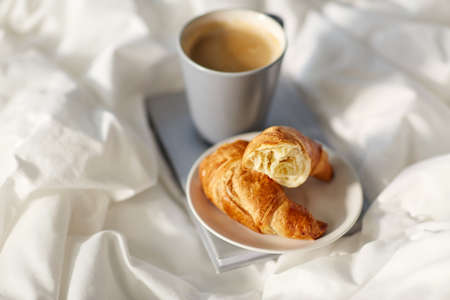 croissants, cup of coffee and book in bed at home