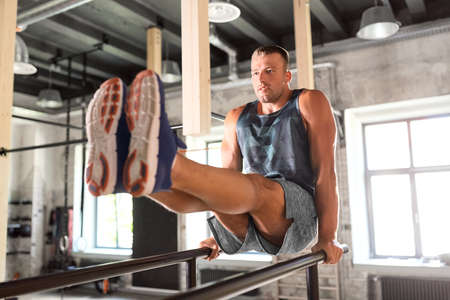 man flexing abs on parallel bars in gym