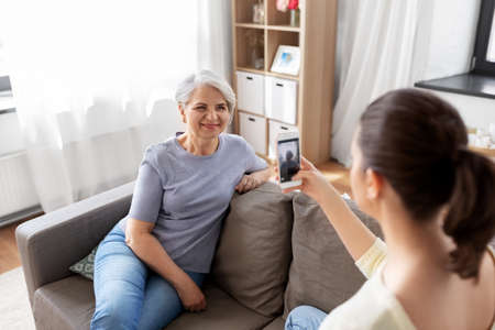 adult daughter photographing senior mother at home