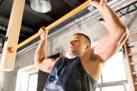 man exercising on bar and doing pull-ups in gym