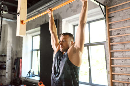 man exercising on bar and doing pull-ups in gym