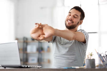 happy man with laptop stretching at home officeの写真素材