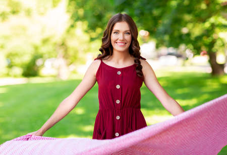 happy woman spreading picnic blanket at parkの写真素材