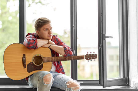 young man with guitar sitting on windowsill