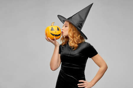 woman in halloween costume of witch kisses pumpkin