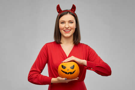 woman in halloween costume of devil with pumpkinの写真素材