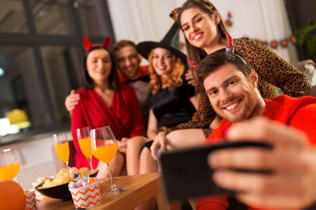 happy friends in halloween costumes taking selfie