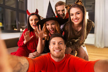 happy friends in halloween costumes taking selfie