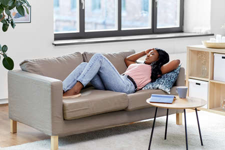 tired african american woman lying on sofa at homeの写真素材