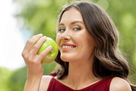 happy woman eating green apple at summer parkの写真素材