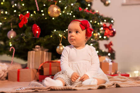 baby girl at christmas tree with gifts at homeの写真素材