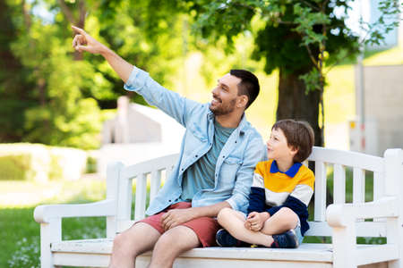 father showing something to son sitting on benchの写真素材