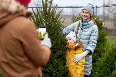 family taking picture of christmas tree at marketの写真素材