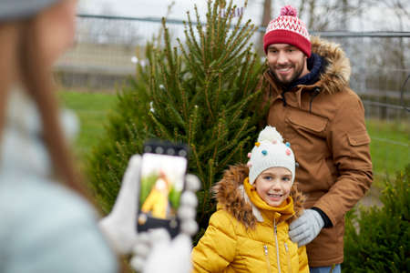 family taking picture of christmas tree at market