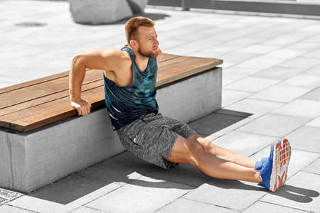 young man doing triceps dip on city street