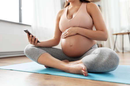happy pregnant woman with phone doing yoga at homeの写真素材