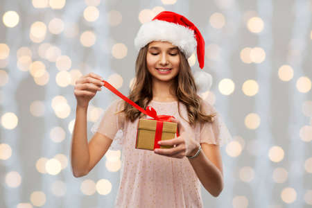 teenage girl in santa hat opening christmas gift