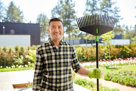 happy middle-aged man with leaf rake at garden