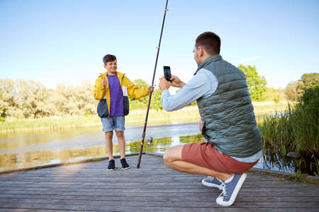 father photographing son with fishing rod on river