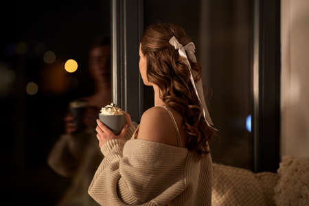 woman holding mug with whipped cream at night