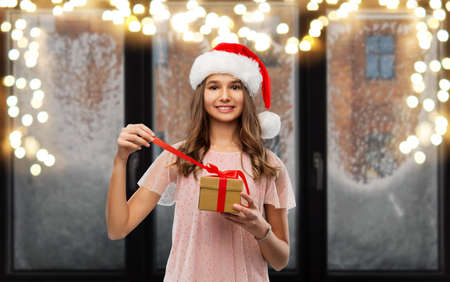 teenage girl in santa hat opening christmas gift