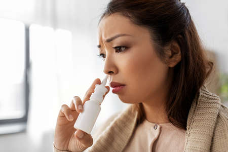 sick asian woman with nasal spray medicine at homeの写真素材