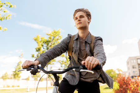 teenage boy with earphones and bag riding bicycleの写真素材