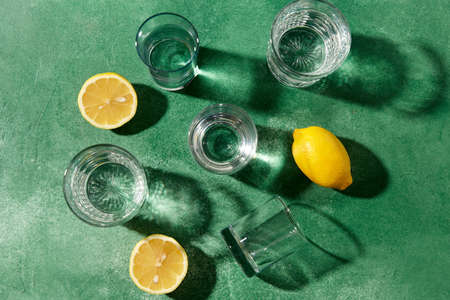 glasses with water and lemons on green backgroundの写真素材