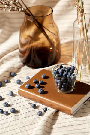 cup of blueberry, book and dried flowers in vases