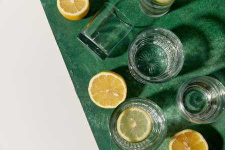 glasses with water and lemons on green background